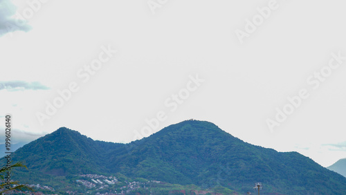 A serene rural landscape featuring a lush green mountain under a bright sky, with farmland in the foreground and scattered trees across the countryside.