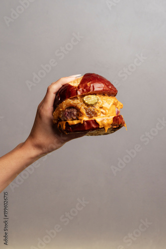 A hand holding a juicy cheeseburger with melted cheese in realistic style on a neutral background, concept of tasty fresh food