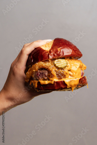 Hand holding a messy cheeseburger in clean photo style on grey background, presenting concept of indulgence