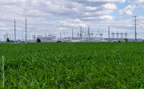 View of new Data Center in Hutto, Texas, behind field with crops. Electrical towers and power lines stretch to the horizon under a cloudy sky.