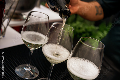 Close-up of sparkling wine being poured into three glasses, bubbles rising as a bartender serves a celebratory drink in a stylish bar setting.