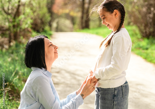 Tablou pe pânză Happy mother and little daughter holding hands and looking into each other's eyes while relaxing in a sunny summer park