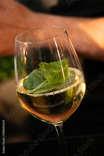 Close-up of sparkling white wine with fresh mint leaves in a glass, glowing in warm light, evoking a refreshing, elegant cocktail moment in a cozy bar setting.