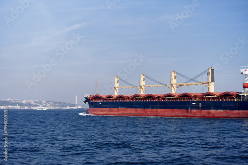 Fotografija Large bulk cargo ship sailing on the Bosphorus with Istanbul shoreline and suspension bridge in the distance under a blue sky