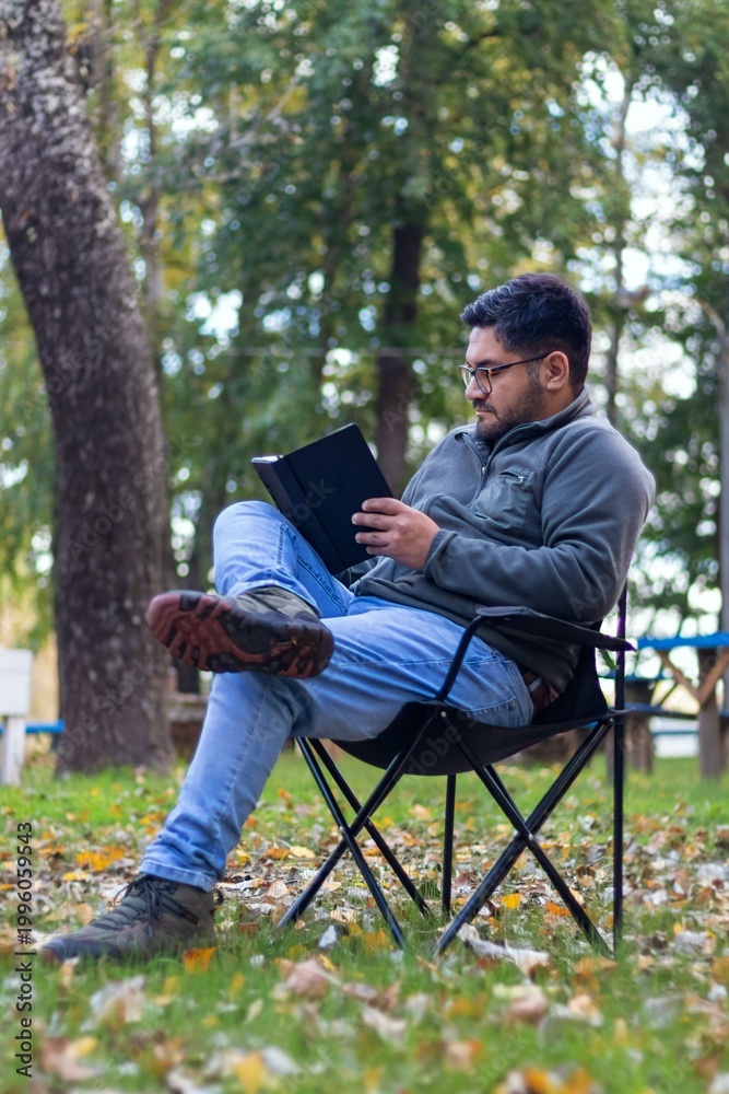 Fototapeta premium A latino man on vacation sitting in nature reading a book