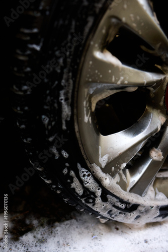 Fotografi Cleaning car wheel with soap and water in a backyard during a sunny afternoon The suds are visible on the shiny rim