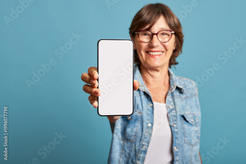 Latina senior woman showing blank smartphone screen on blue background