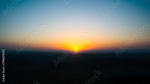 Golden rays of dawn breaking over the horizon into a deep blue pre-dawn sky.