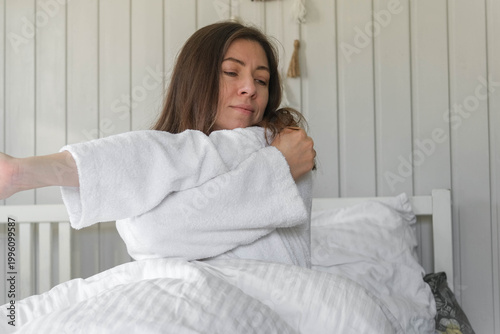 Woman stretching in bed, morning light, soft robe, relaxed expression, cozy white bedding, calm bedroom, waking up before remote work, natural light from the window, quiet moment of self-care. Banner