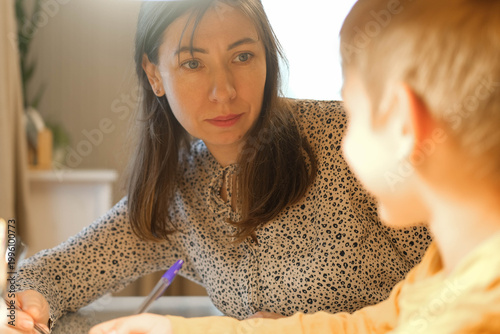 A mother helping her son with his studies. Homework assistance. Warm lighting. A cozy atmosphere for family learning. A focused student's pose. A scene of studying before bed. Space for text. Banner.
