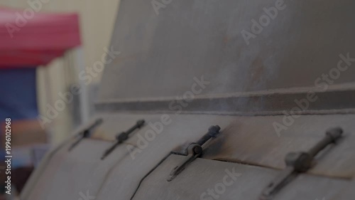 This close up video shows a side view of smoke coming out of a large industrial bbq smoker in slow motion.