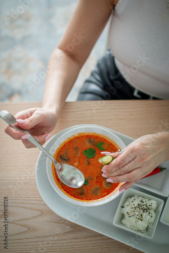 Female hands squeezing lime into tom yum soup served with rice on a white platter over wooden table