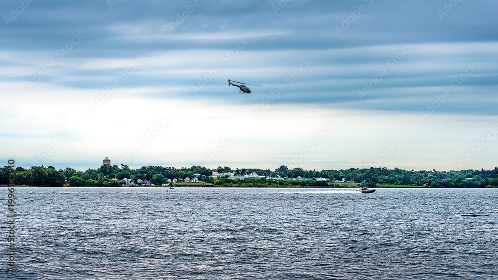 Fototapeta premium Helicopter flying overhead of a speedboat under a stormy sky.