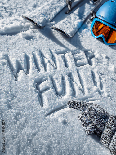 words WINTER FUN Written in the soft snow with a snow glove, the fronts of two skis and a Helmet and goggles