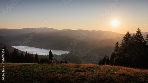 Ein ruhiger Moment in der Natur: Eine Person genießt den Sonnenuntergang über dem Titisee im Schwarzwald und blickt über die sanften Hügel und Wälder im goldenen Licht der Abendstunden.