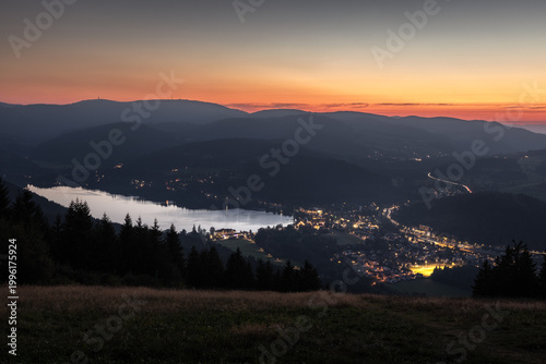 Abendstimmung über dem Titisee im Schwarzwald vom Hochfirstturm aus. Stimmungsvolle Dämmerung am Titisee im Schwarzwald mit Blick vom Hochfirstturm auf See, Berge und beleuchtete Ortschaft.
