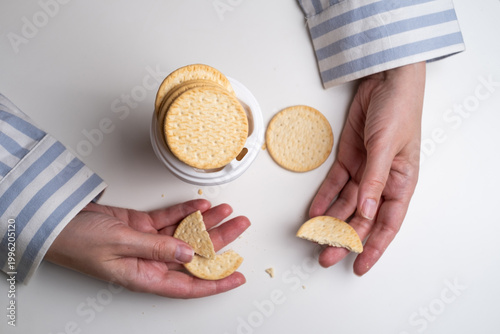 Woman holding broken cookie near paper coffee cup on white table. Snack break concept. 