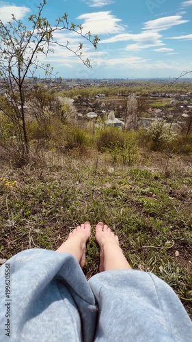 Bare feet resting on grass with a view of a town in the distance
