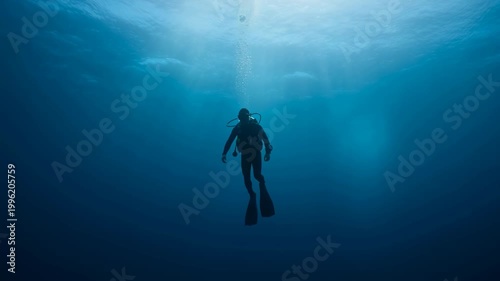 Scuba diver descending into deep blue ocean water. Man in wetsuit swimming in dark sea with oxygen bubbles rising to surface. Underwater exploration sequence, nautical adventure, extreme water sport
