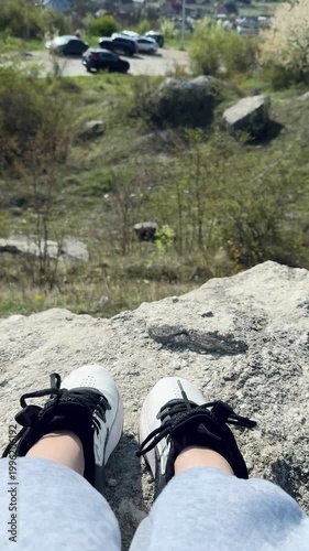 Feet in white sneakers resting on rocks with a distant view of parked cars