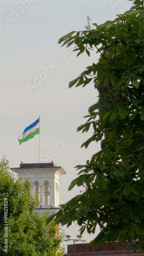 Clock tower with Uzbekistan flag in Tashkent surrounded by trees