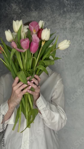 Static shot of person holding and hiding behind bouquet of pink white red tulips in studio portrait