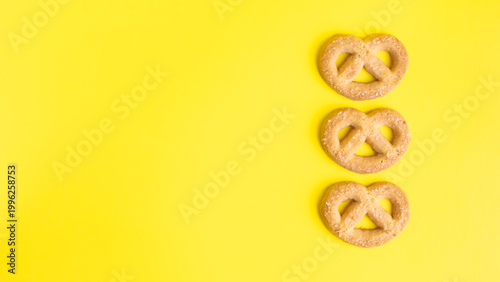 Flat lay of three sweet Swedish pretzel cookies on bright yellow background with empty copy space for text.

