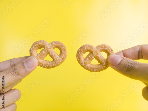 Two hands holding two sweet Swedish pretzel cookies on a yellow background. Delicious bakery pastry for food advertisement
