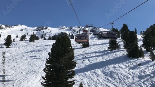 Riding a ski lift up a snow-covered mountain with evergreen trees under a clear blue sky.