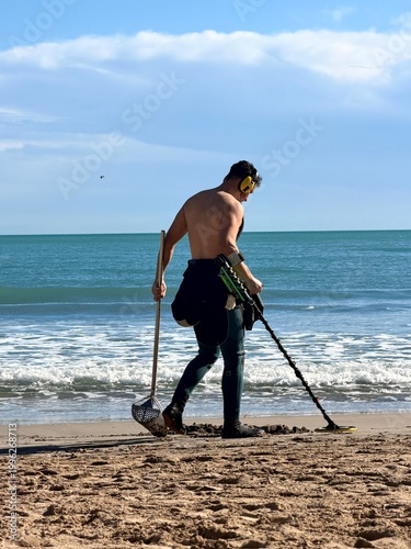Man using metal detector on beach searching for treasure by the sea