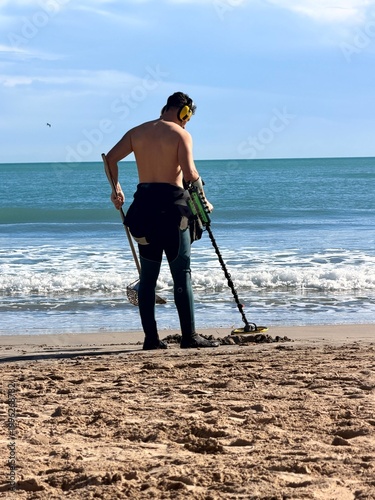 Man metal detecting on beach with ocean waves and peaceful coastal scene
