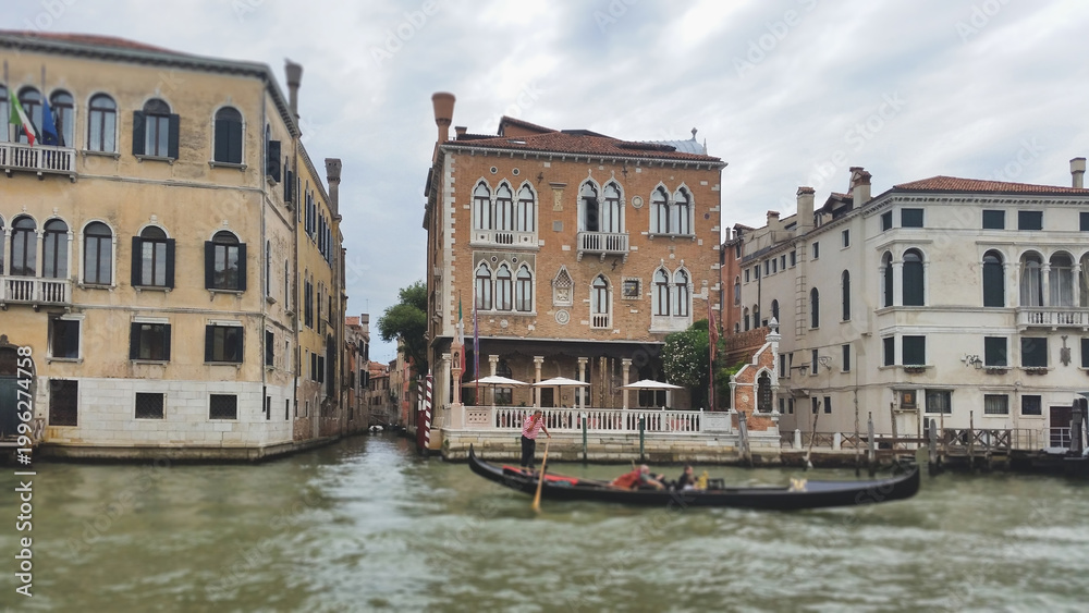 Obraz premium A traditional black gondola with tourists passing historic Venetian palaces along the Grand Canal in Venice