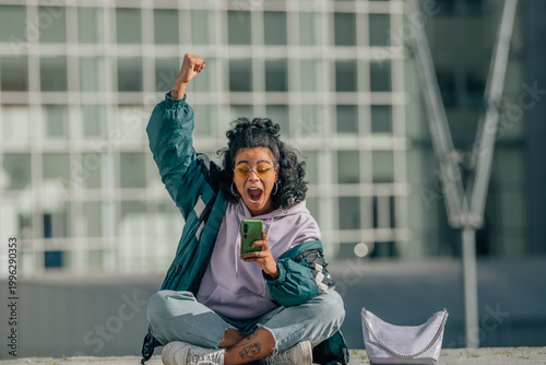 Tableau sur toile A euphoric young woman with curly hair raises her fist in a victory gesture whil