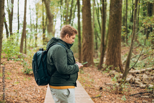 A man in a forest is looking for a way using a mobile navigator - to get lost in the forest. Male explorer looking for connection to the internet or using gps navigator app on phone