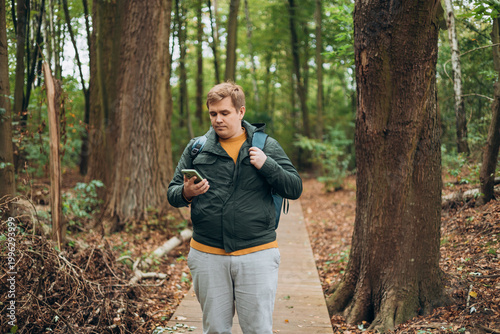 A man in a forest is looking for a way using a mobile navigator - to get lost in the forest. Male explorer looking for connection to the internet or using gps navigator app on phone