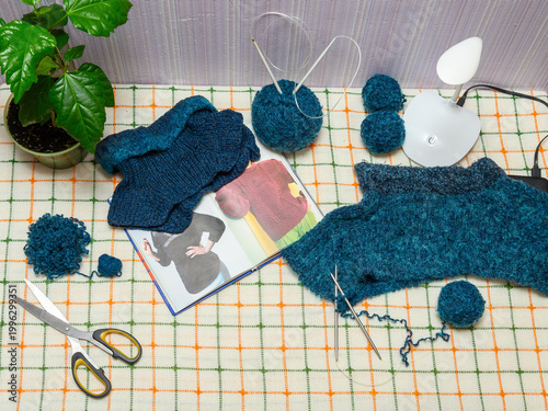 top view of a table with blue yarn knitting and an instruction book by a plant