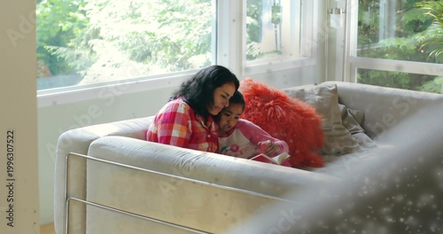 Valokuva Reading mother in plaid shirt, daughter in pink pajamas holding book at home, or