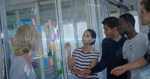 Discussing five coworkers in striped shirt pointing at glass planning wall, with Post-it notes
