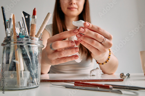 Schilderij op canvas Young woman artist sculpting a small white figure from polymer clay at her home