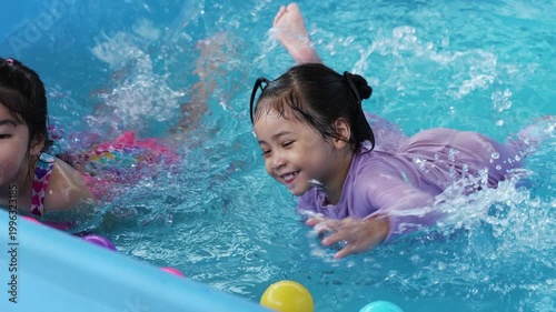 slow motion of happy preschool child girl playing together with her sister in outdoor portable swimming pool in backyard at home