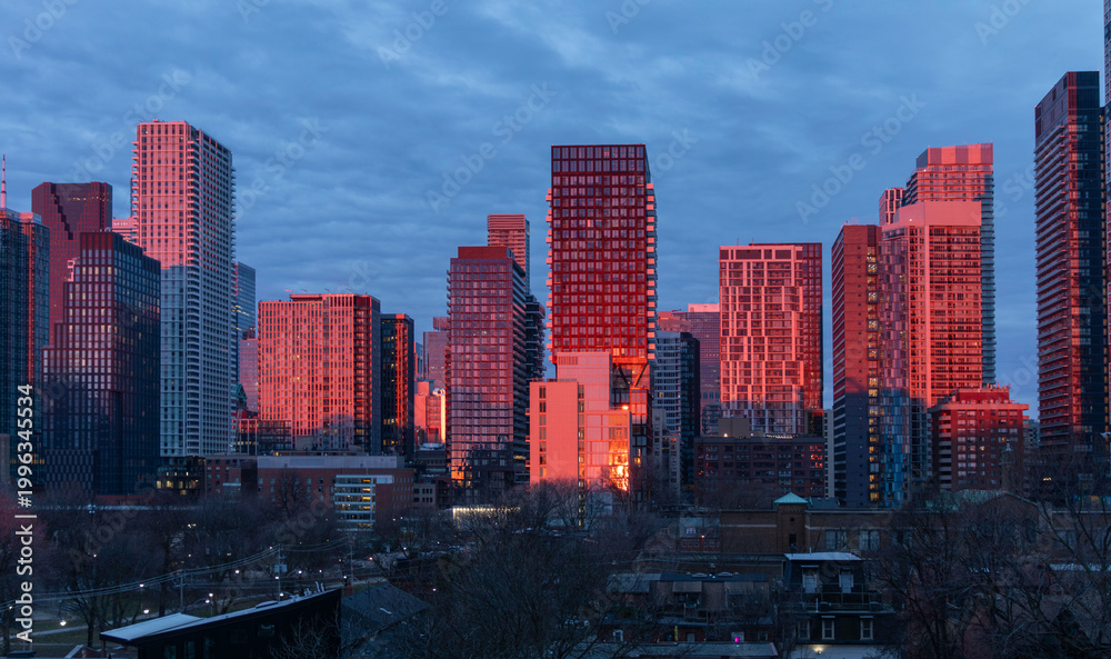 Fototapeta premium Newly completed condos and other downtown Toronto buildings glow fiery red in the dawn sunlight.