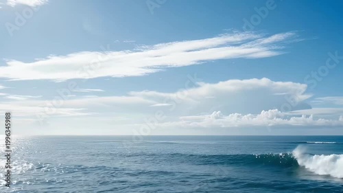 Vast ocean landscape with horizon line and breaking wave under a clear blue sky with white clouds