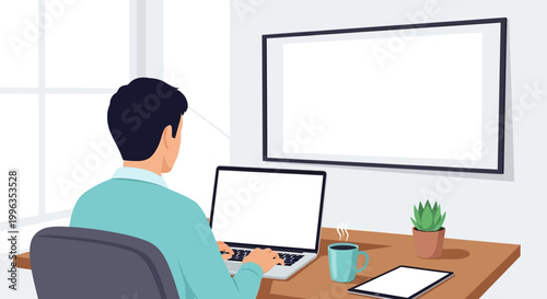 A young professional working on a laptop at a desk with a large blank screen in front.