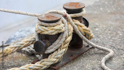 Bild auf Leinwand Rusty metal bollard securely holding thick mooring ropes on a concrete pier, rep