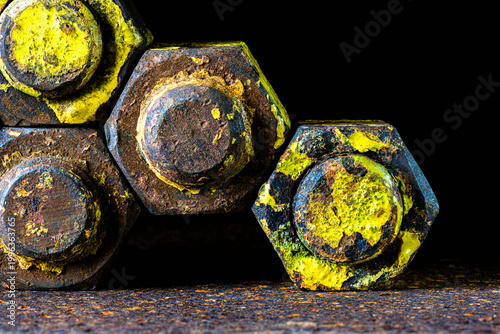 Close-up of thick old bolts with nuts on a rusty steel surface, in dark industrial environment