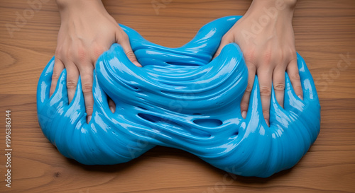 Blue candy dough stretched by hands on wooden table, glossy sugar paste texture, vibrant taffy kneading, edible slime concept, sensory food play, sweet fondant manipulation.