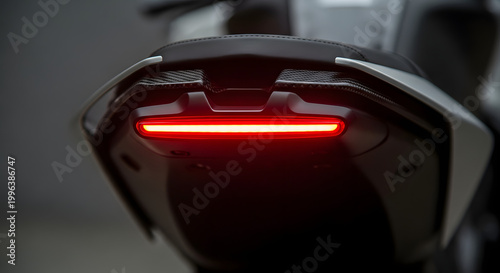 A close-up image of a sleek, black motorcycle taillight, glowing red in a dark studio with natural lighting.