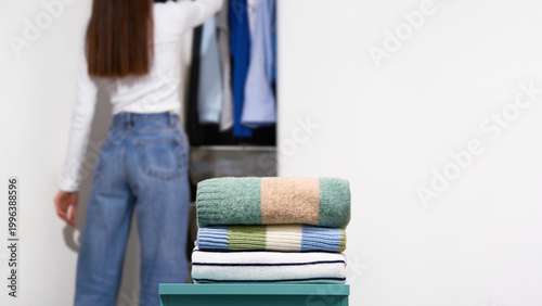 Tableau sur toile Folded knitted sweaters with woman near open wardrobe on light gray background