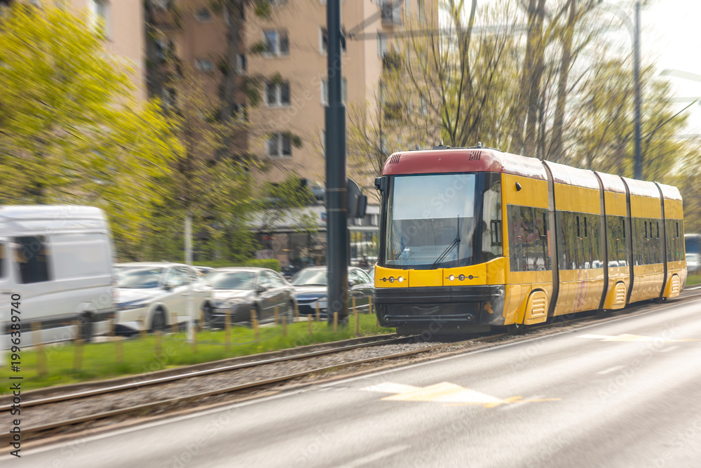 Obraz premium Yellow tram moving along city rails. Urban public transport in daily motion.