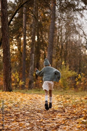 Caucasian Girl Running Away Along Leafy Trail, Cardigan Swaying And Boots Kicking Leaves, Dynamic Backview Through Golden Trees, Sense Of Youthful Exploration And Freedom, Seasonal Outdoor